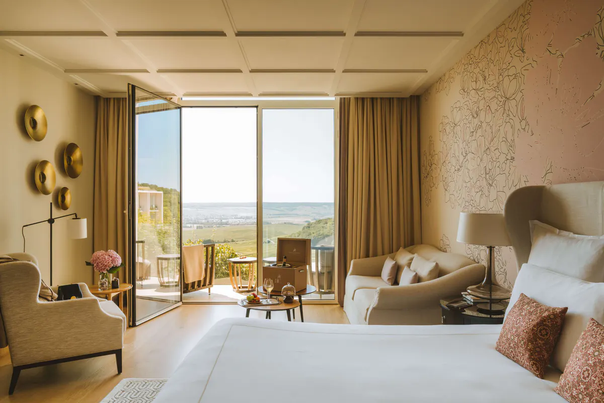 Bedroom with large windows framing green vineyard landscape, gold curtains, and neutral furnishings