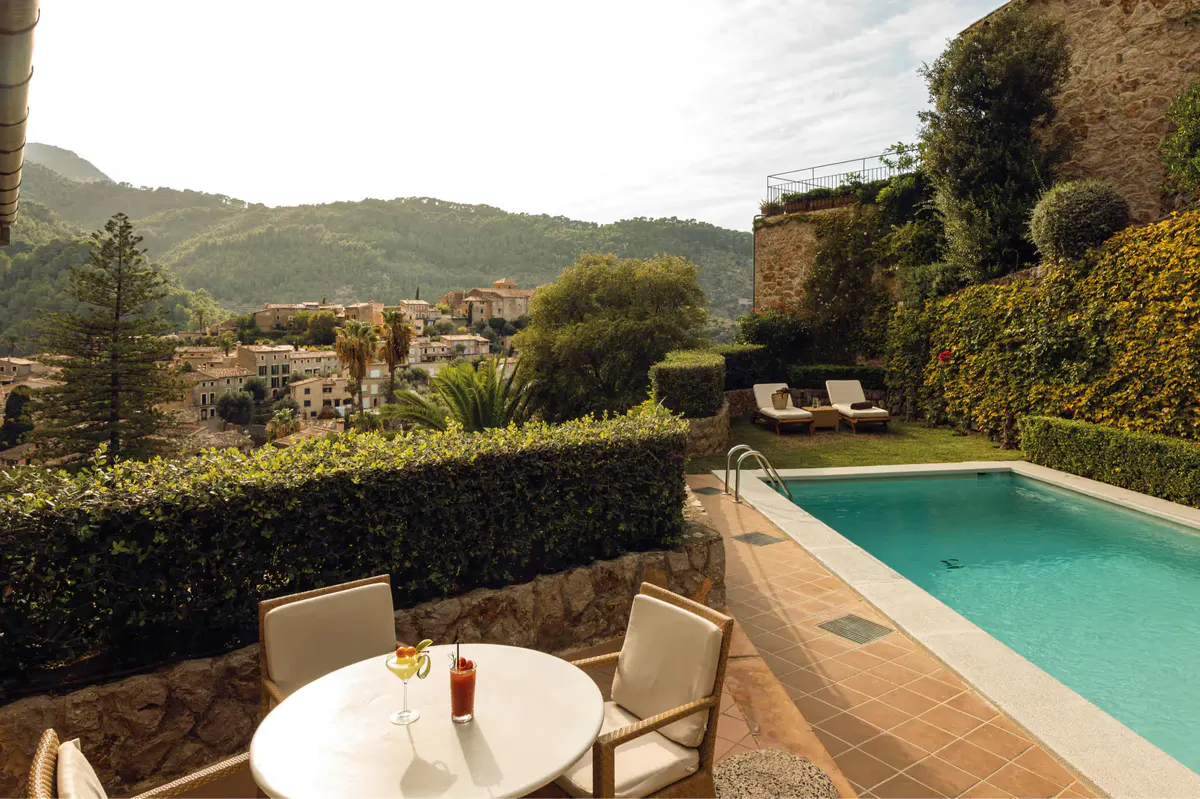 Private terrace overlooking a hillside with turquoise pool, dining table, and mountain backdrop