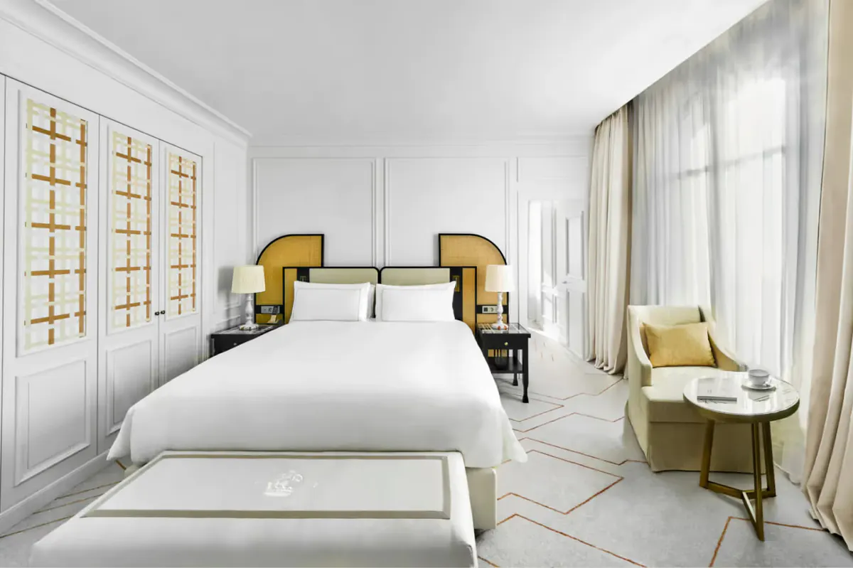 Master bedroom with white bed accented by gold-trimmed nightstands, white wall paneling, and a yellow accent chair