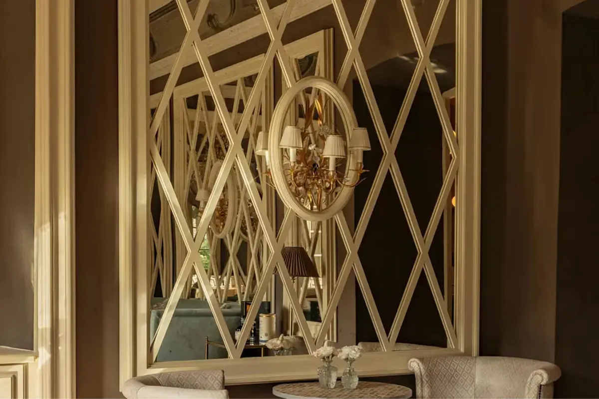 An ornate gold-framed mirror flanked by cream panels with geometric wallpaper
