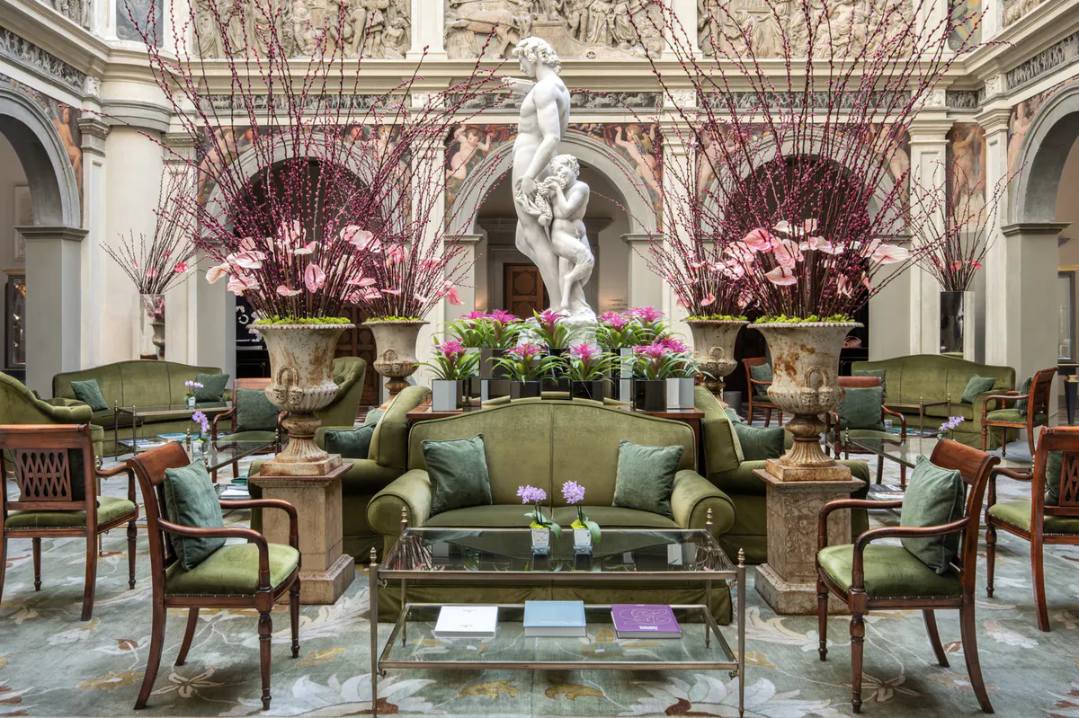 Grand lobby with soaring ceilings, classical frescoes, green upholstered seating, and floral arrangements