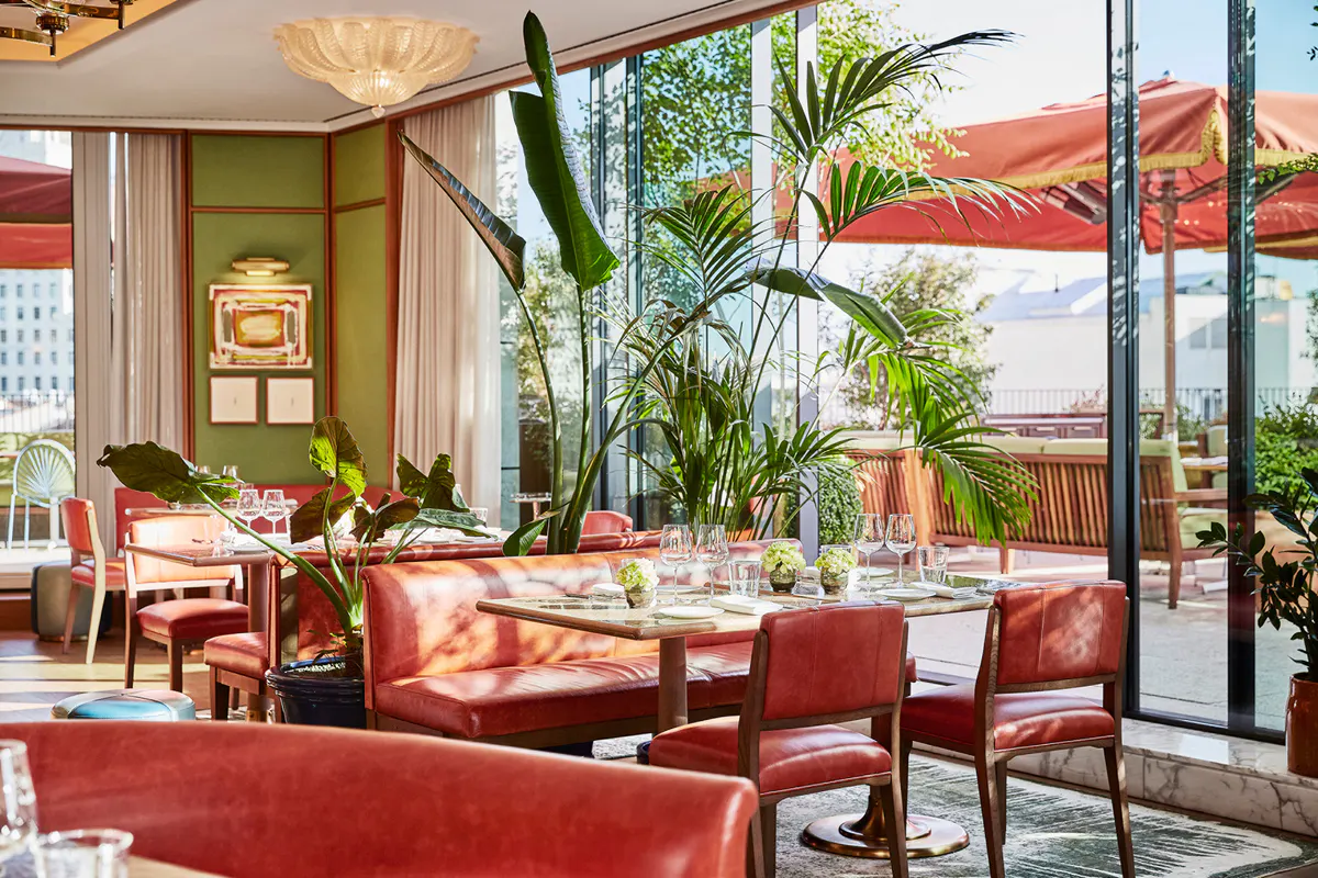 Rooftop dining terrace with coral seating, tropical plants, and skyline views through glass doors