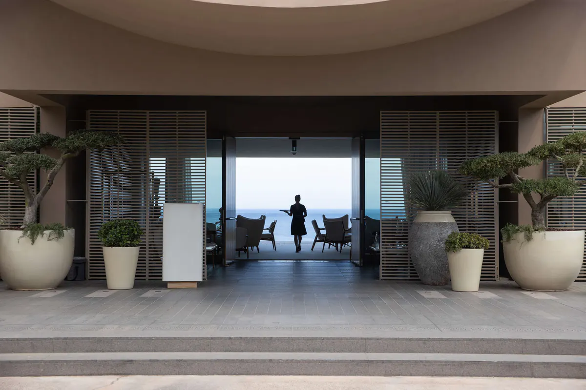 Figures walk through open doors toward a terraced seating area