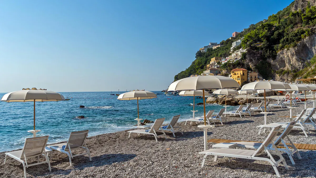 Beach with loungers and umbrellas beside rocky promontory and clear blue water