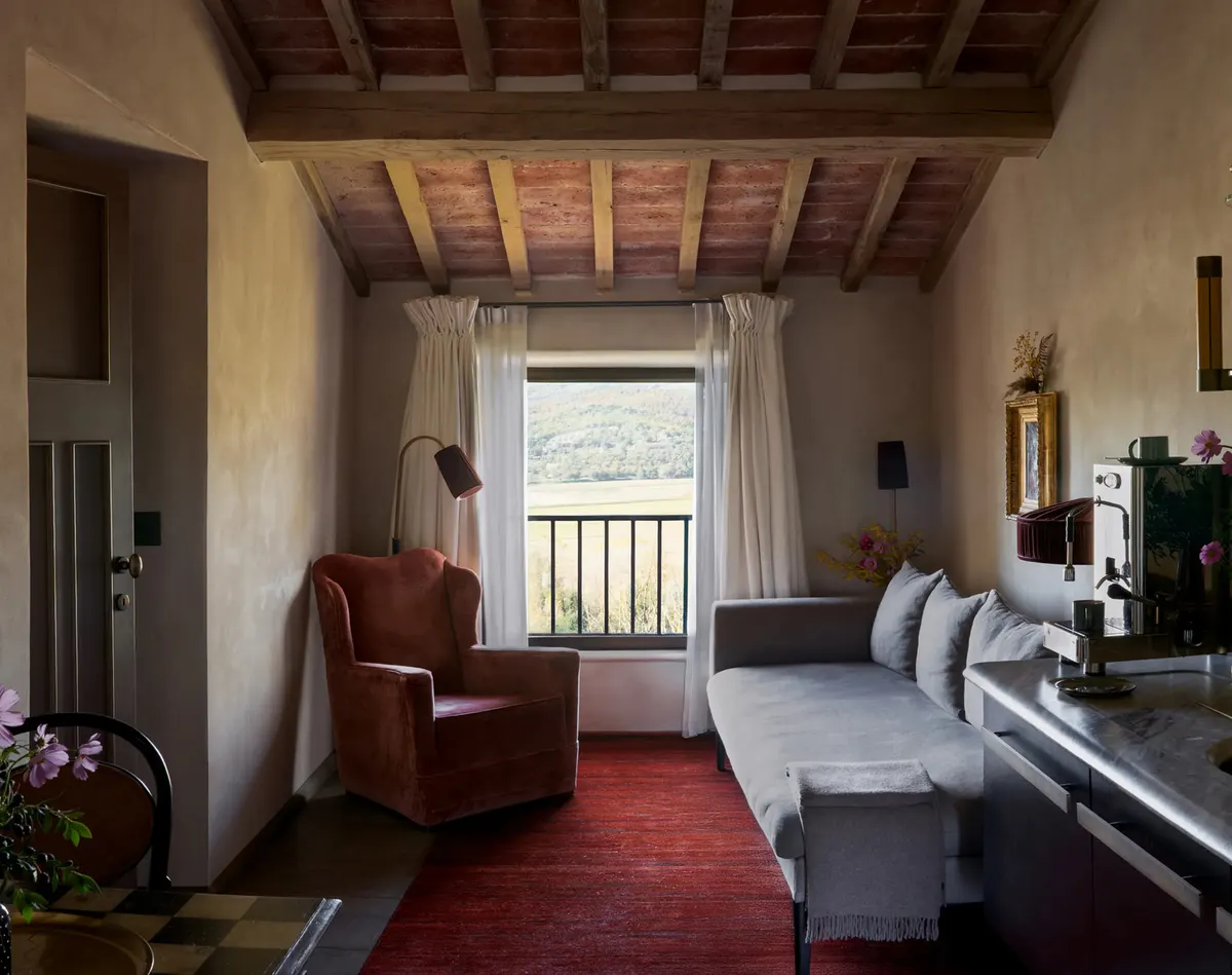 A sitting room framed by a stone archway, with a red rug, an upholstered daybed, and garden light through tall windows