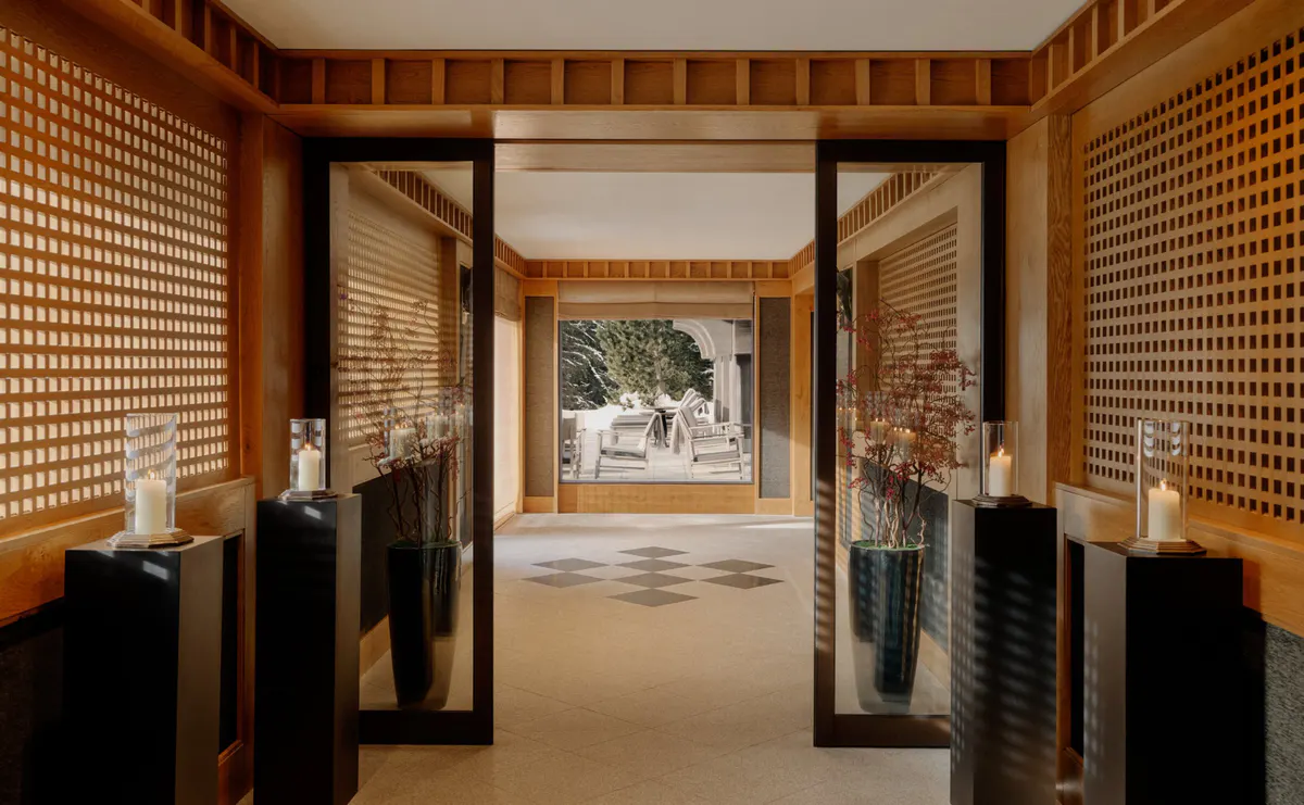 Entry corridor with mirrored screens, candlelit pedestals, and a checkerboard floor leading outside