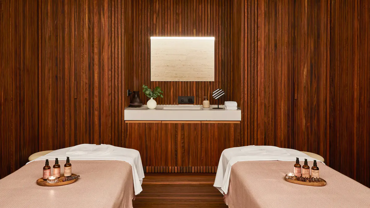 A treatment room with two massage tables, wood paneling, and warm ambient lighting