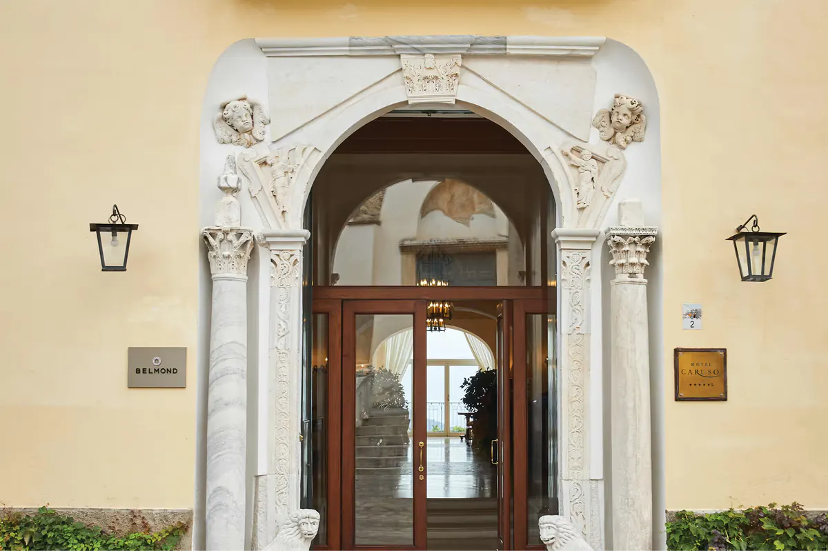 Ornate arched doorway with carved stone columns, dark wood doors, and brass fixtures on cream facade