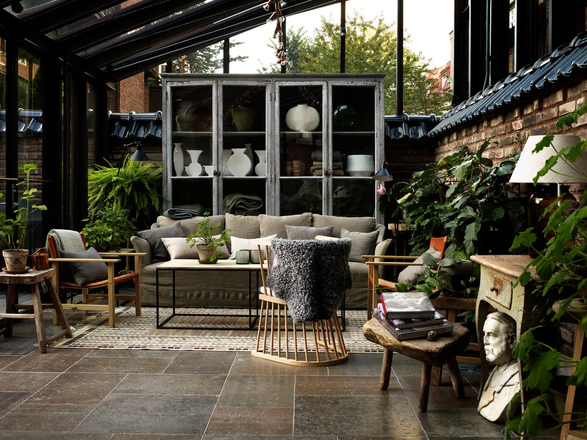 A covered terrace with wooden and rattan furniture, skylights, and potted plants