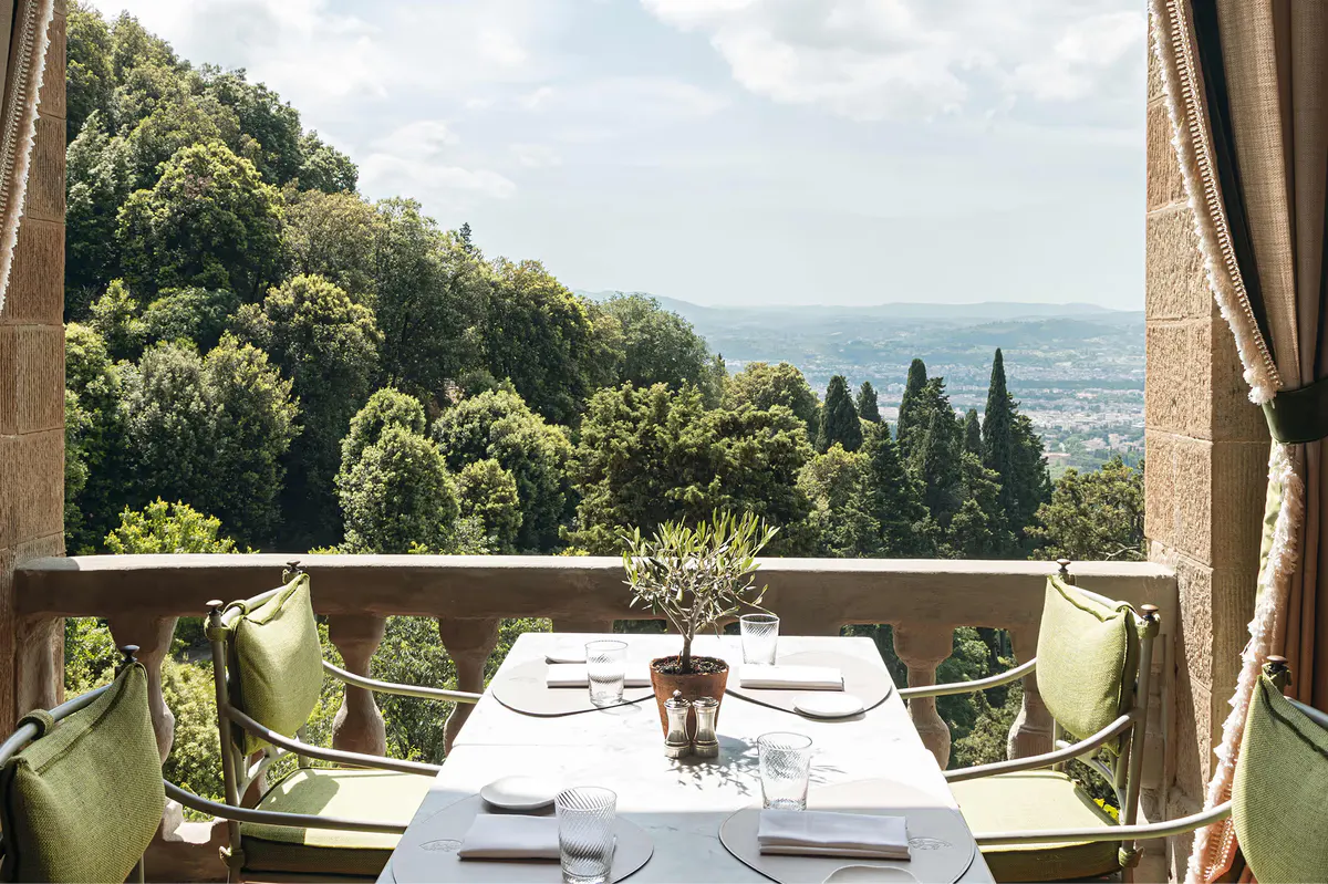 A table set for one on a terrace overlooking forested Tuscan hills and valleys below