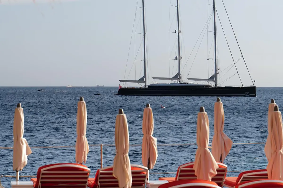Luxury sailing yacht on blue water with striped umbrellas and lounges in foreground