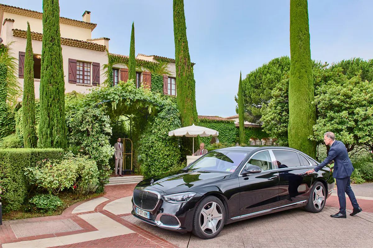 Luxury car departing the château entrance with cypress-lined driveway