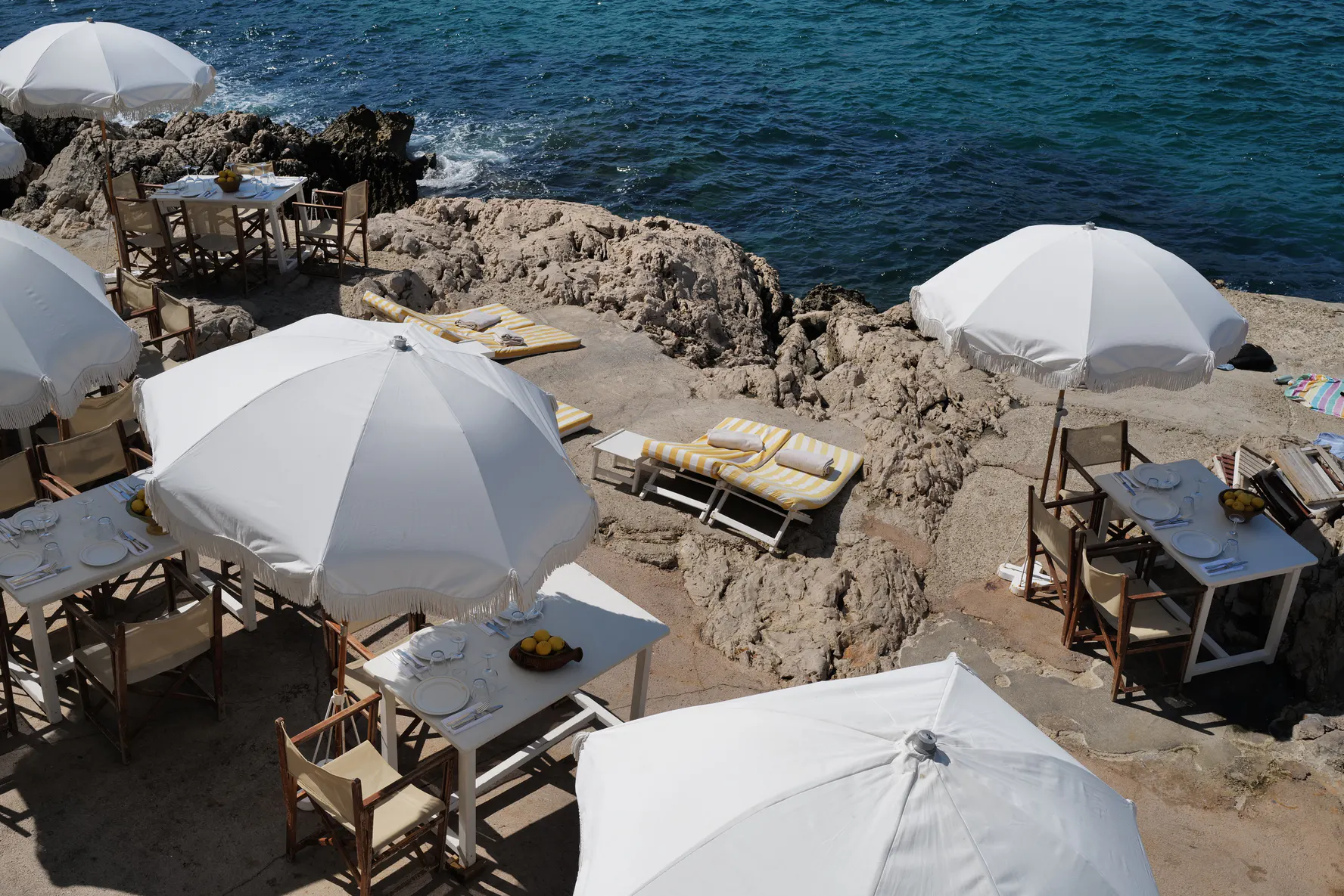The tables, parasols and loungers of Tuba Club spread across the rocks above the sea