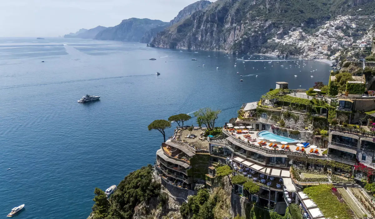 Aerial view of white terraced hotel buildings cascading down cliffs above sparkling turquoise cove