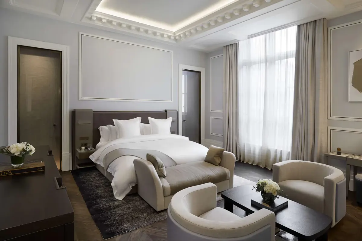 A bedroom with white upholstered headboard, pale furnishings, and two-tone bedside tables