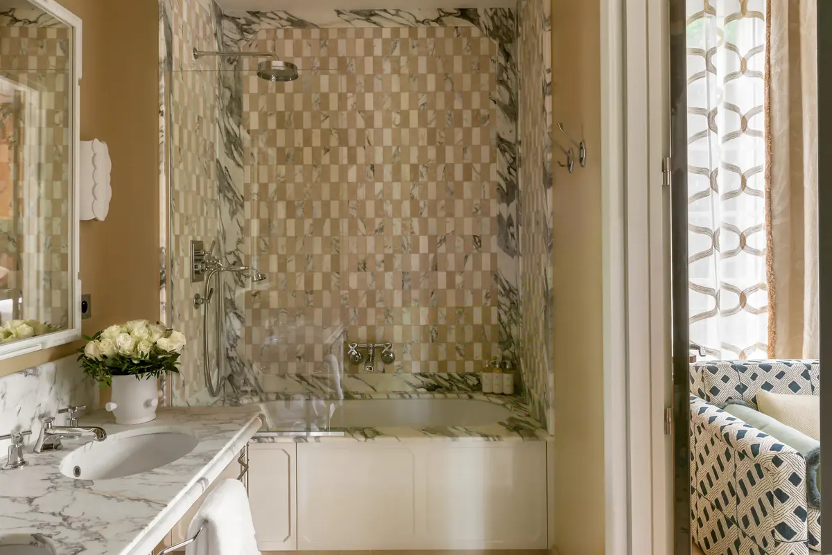 Bathroom with white marble vanity, patterned tile shower enclosure, and brass fixtures