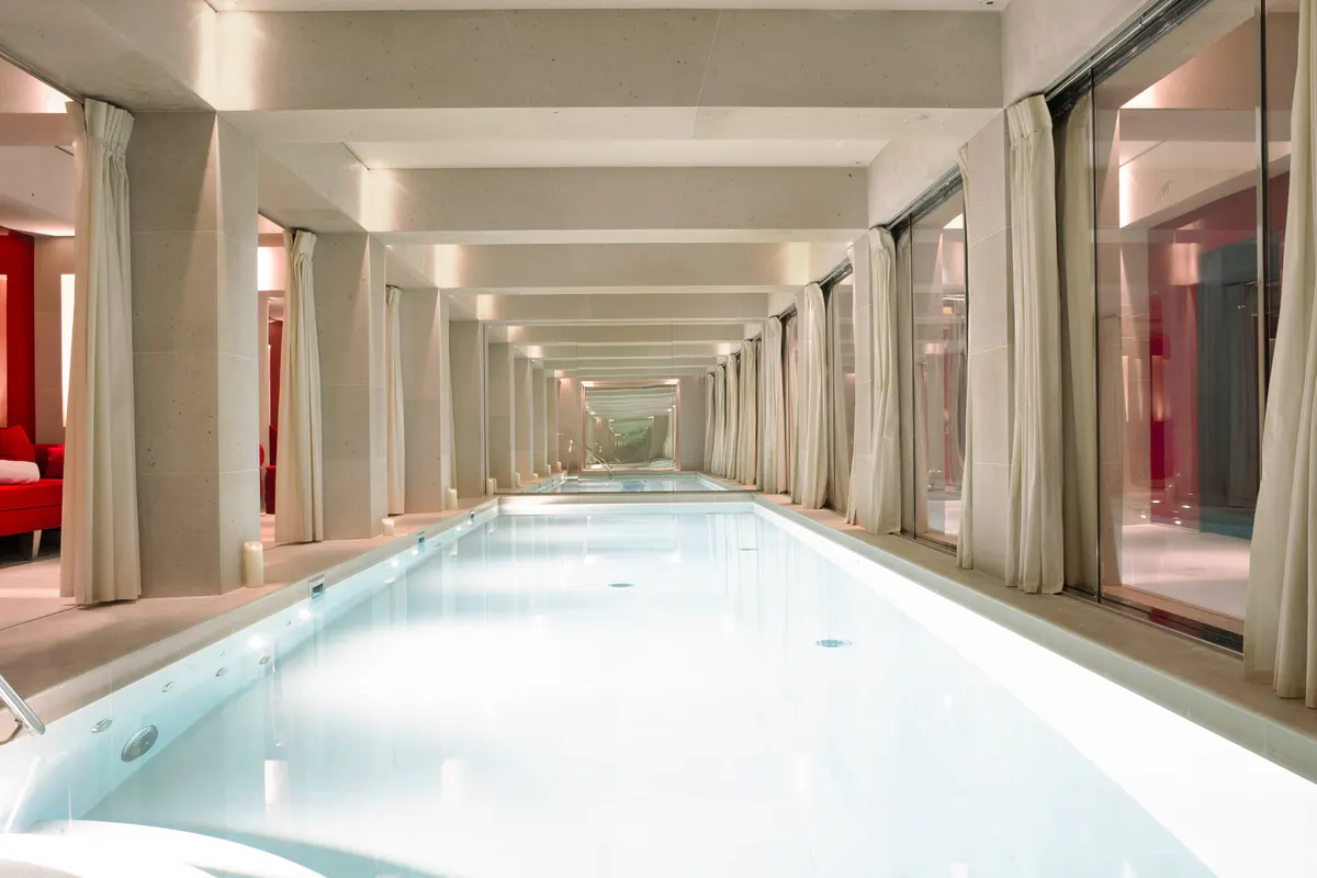 An indoor pool with pale blue water and cream marble columns lining both sides