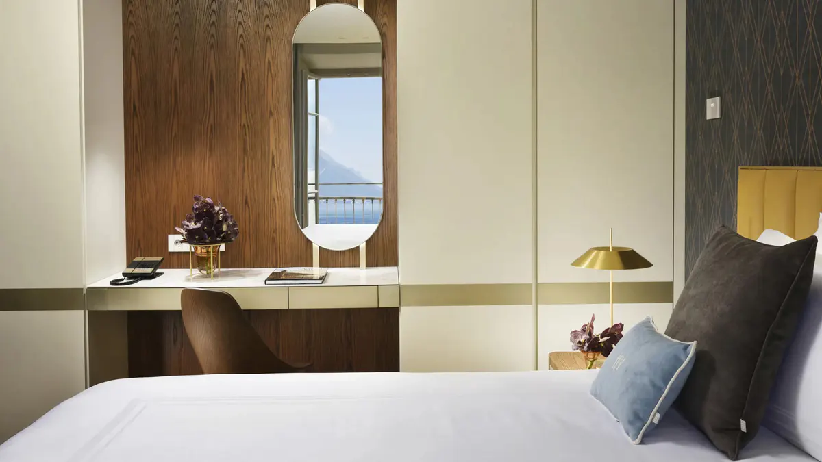 A bedroom with pale walls, natural light from doors, and wood furnishings