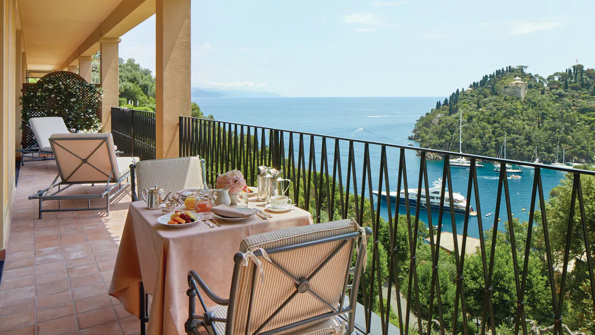 A dining table set on a terrace with sea view, framed by pergola and metal railings