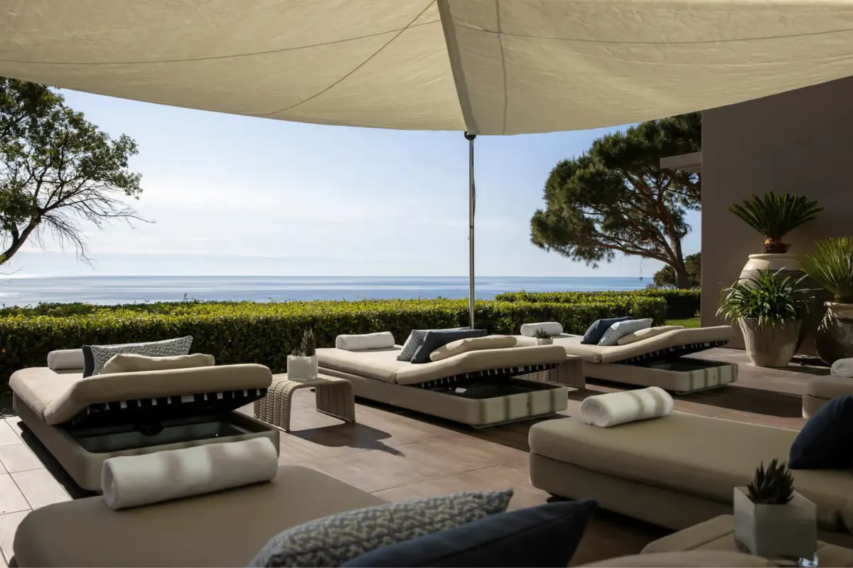 Shaded terrace with layered lounges and sea views beneath umbrellas