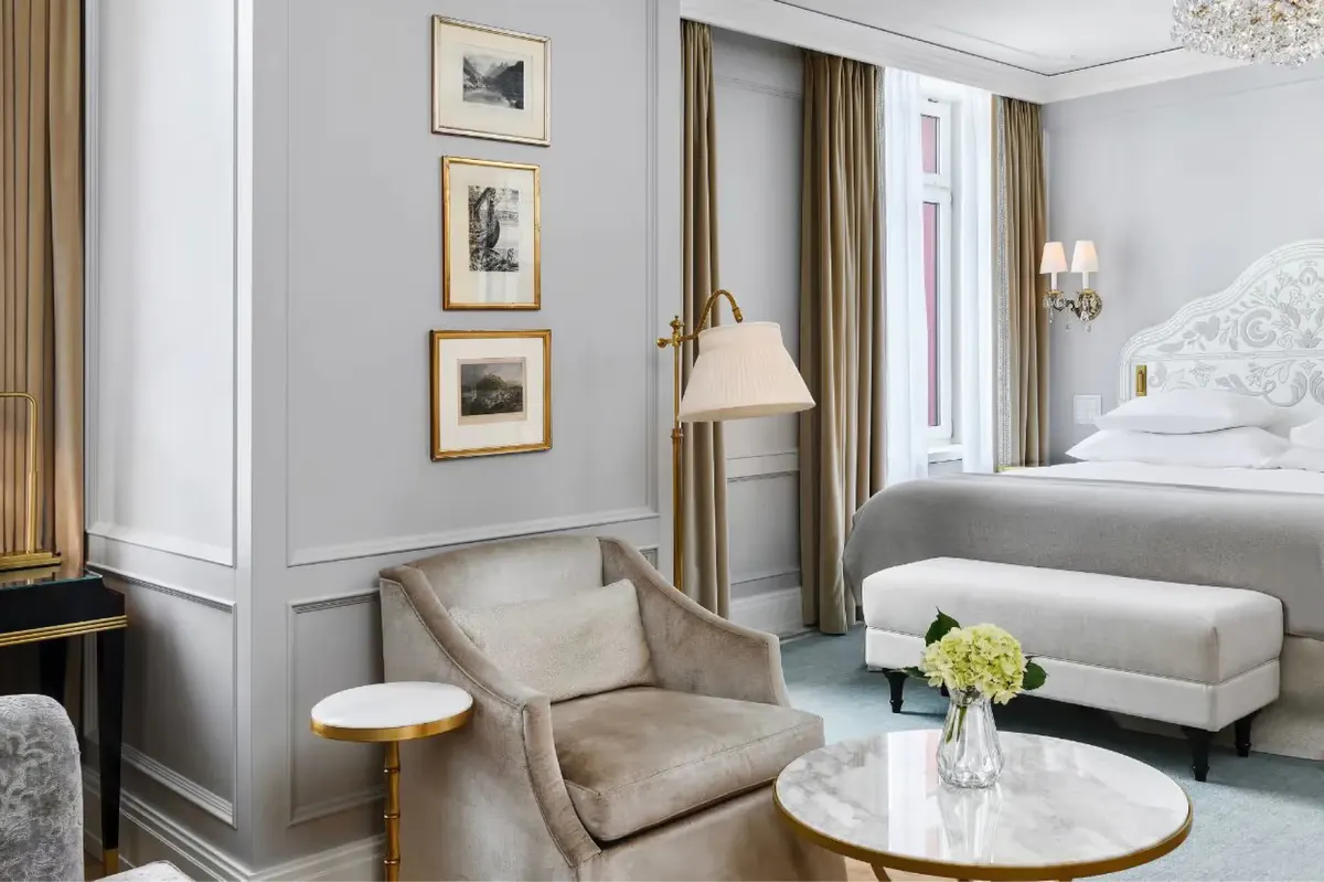 Elegant suite with upholstered armchairs, sofa, framed artwork, and bedside flowers