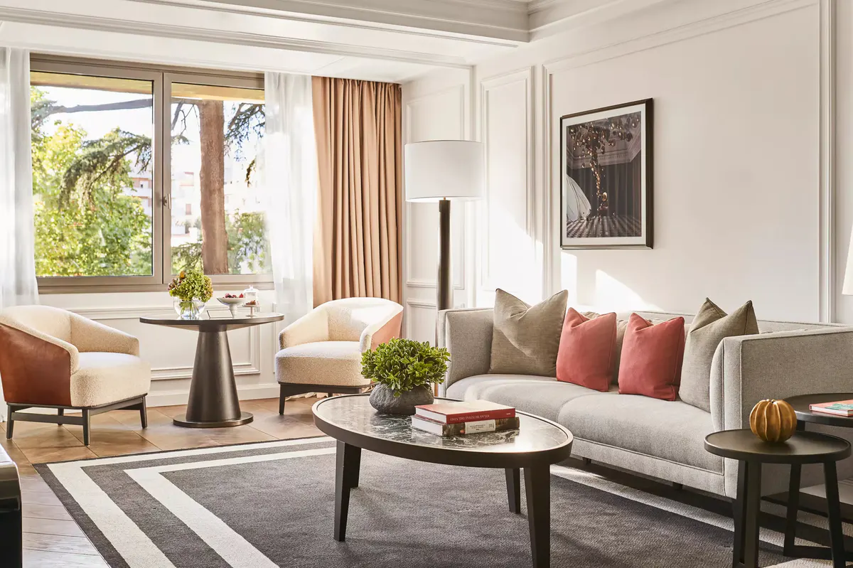 A living room with gray upholstered sofa, gold chandelier, and large windows overlooking the city