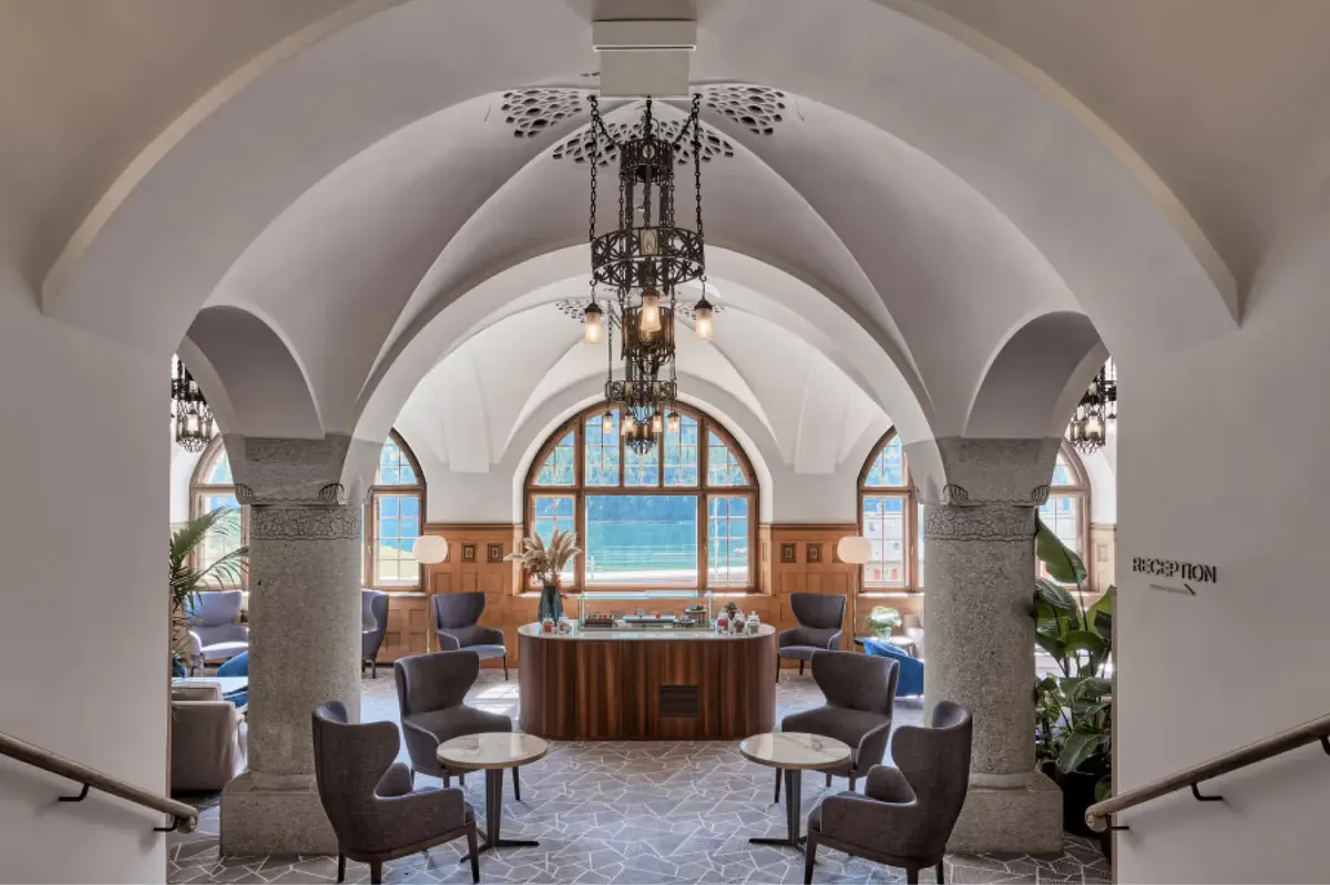 Grand arched hallway with ornate chandeliers, blue window alcoves, and fireplace