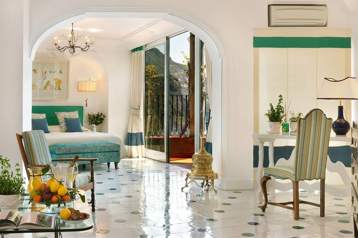 Airy bedroom suite with arched entryway, green velvet seating, marble inlay flooring, and open doors to sea terrace