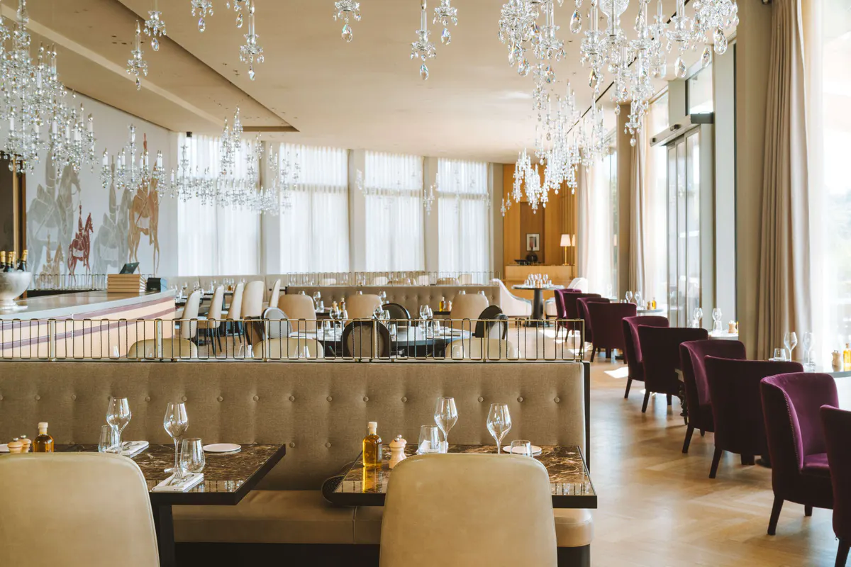 Fine dining room with crystal chandelier, gold ceiling details, and long banquettes in wine tones