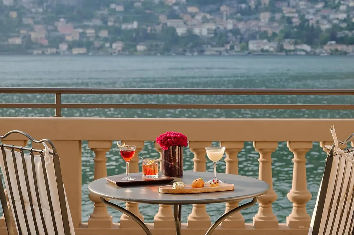Lakeside table set for two with lake views across railing and distant hillside villages