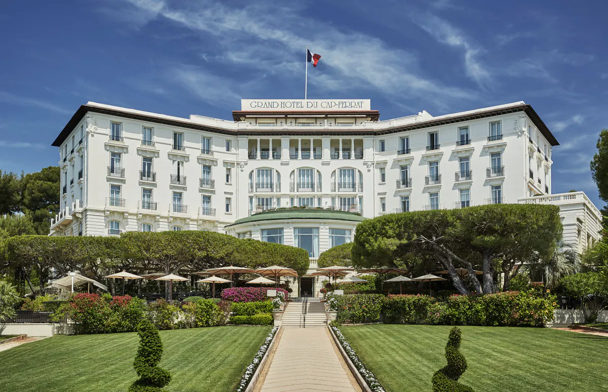 The cream-colored neoclassical facade rises above manicured gardens and lawn