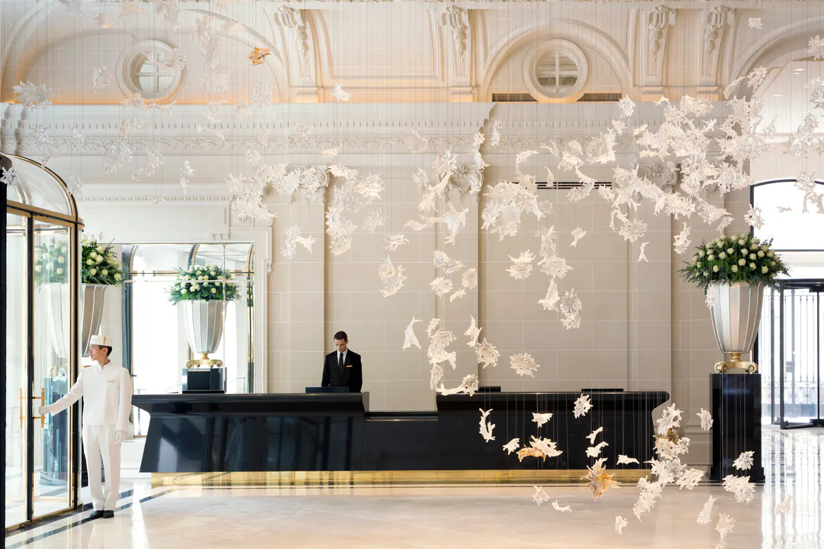 Grand lobby space with cream ceilings, gilded details, hanging installations, and a reception desk