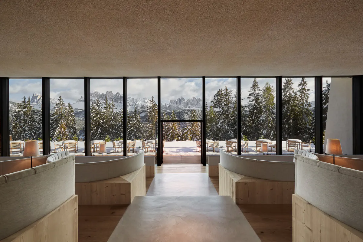 A dining room with floor-to-ceiling windows framing mountains, light wood and concrete finishes, and neutral furnishings