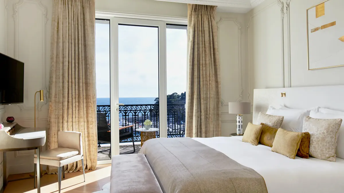 Bedroom with bed facing open balcony with sea view, earth-tone furnishings