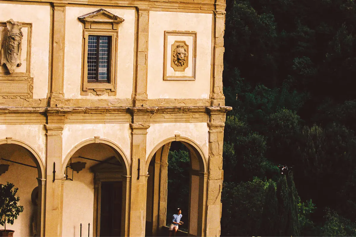 Cream-colored Renaissance facade with arched columns, carved stone ornaments, and dense ivy covering the hillside