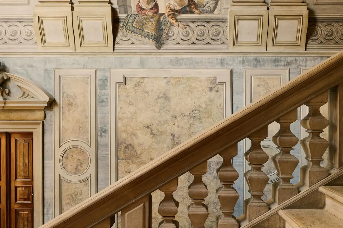 A marble staircase with ornamental railings, painted ceiling with classical medallions, and cream walls