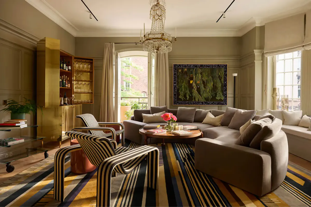 A living room with taupe sofa, striped rug, artwork, and natural light from windows
