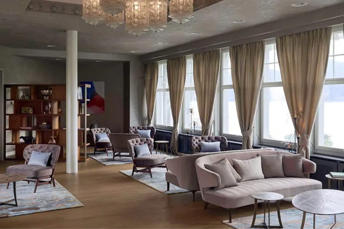 Contemporary lounge with large windows, cream furnishings, wooden bookcase, and Alpine mountain view