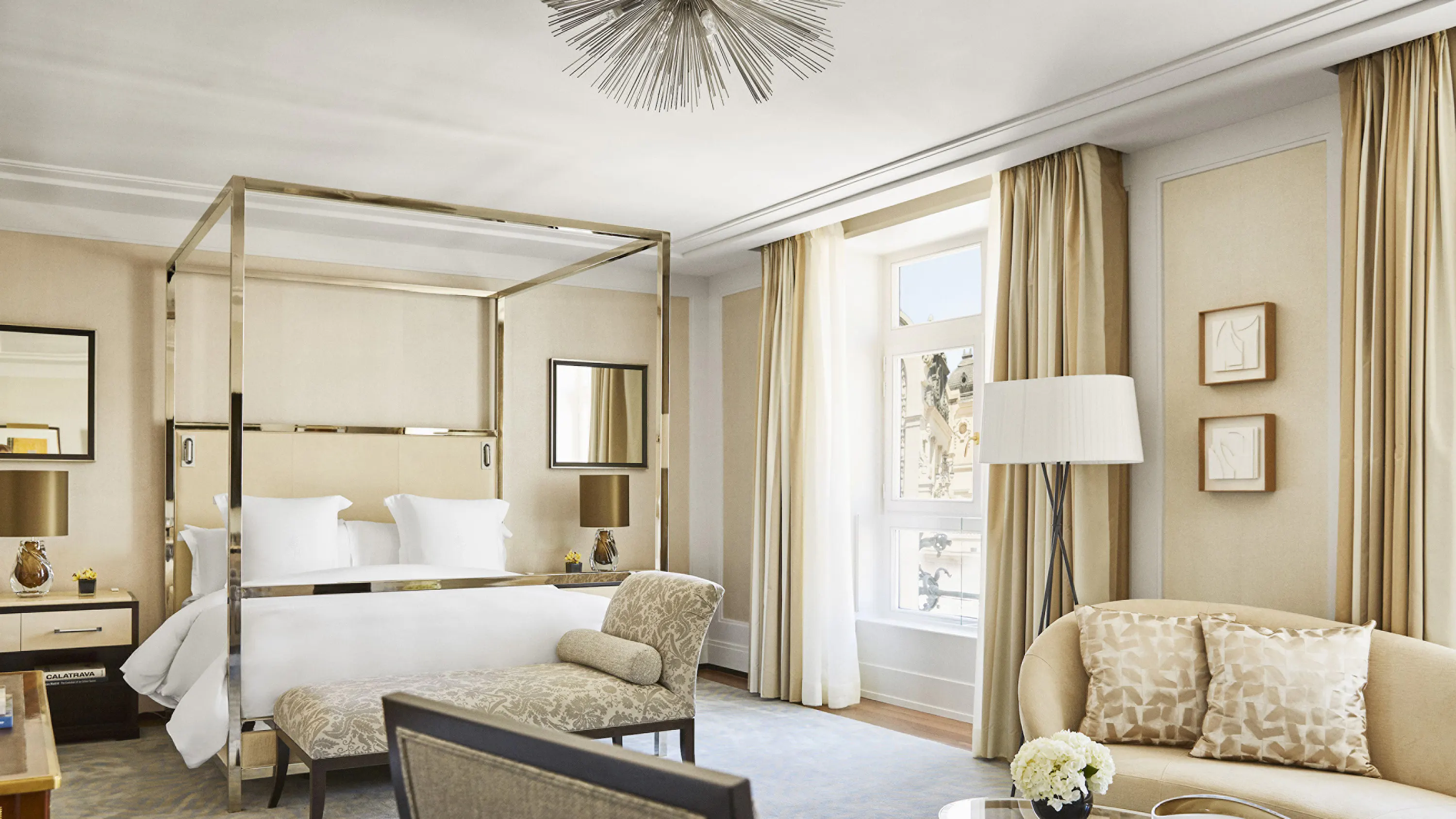 A canopy bed with gold framing and marble accents in a neutral suite with cream drapes and arched ceiling