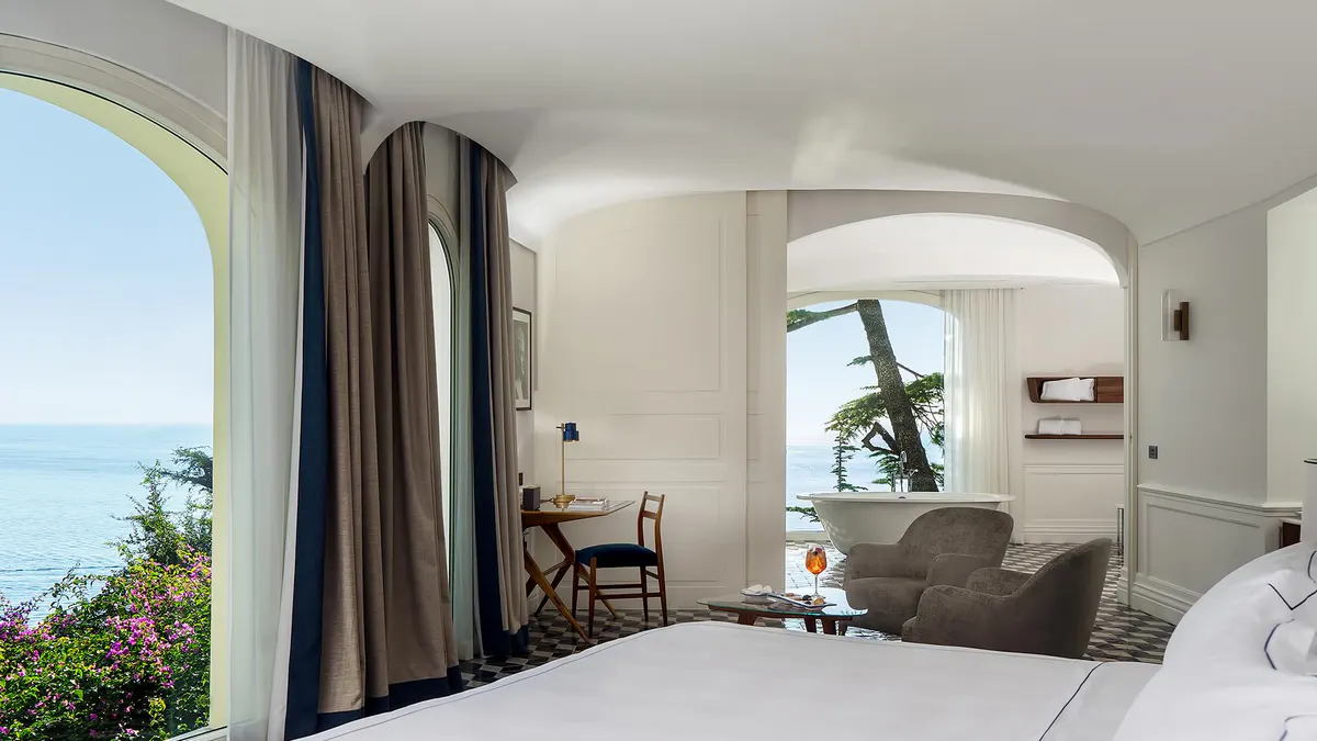 Bedroom with curved glass doors opening to seating area with sea views