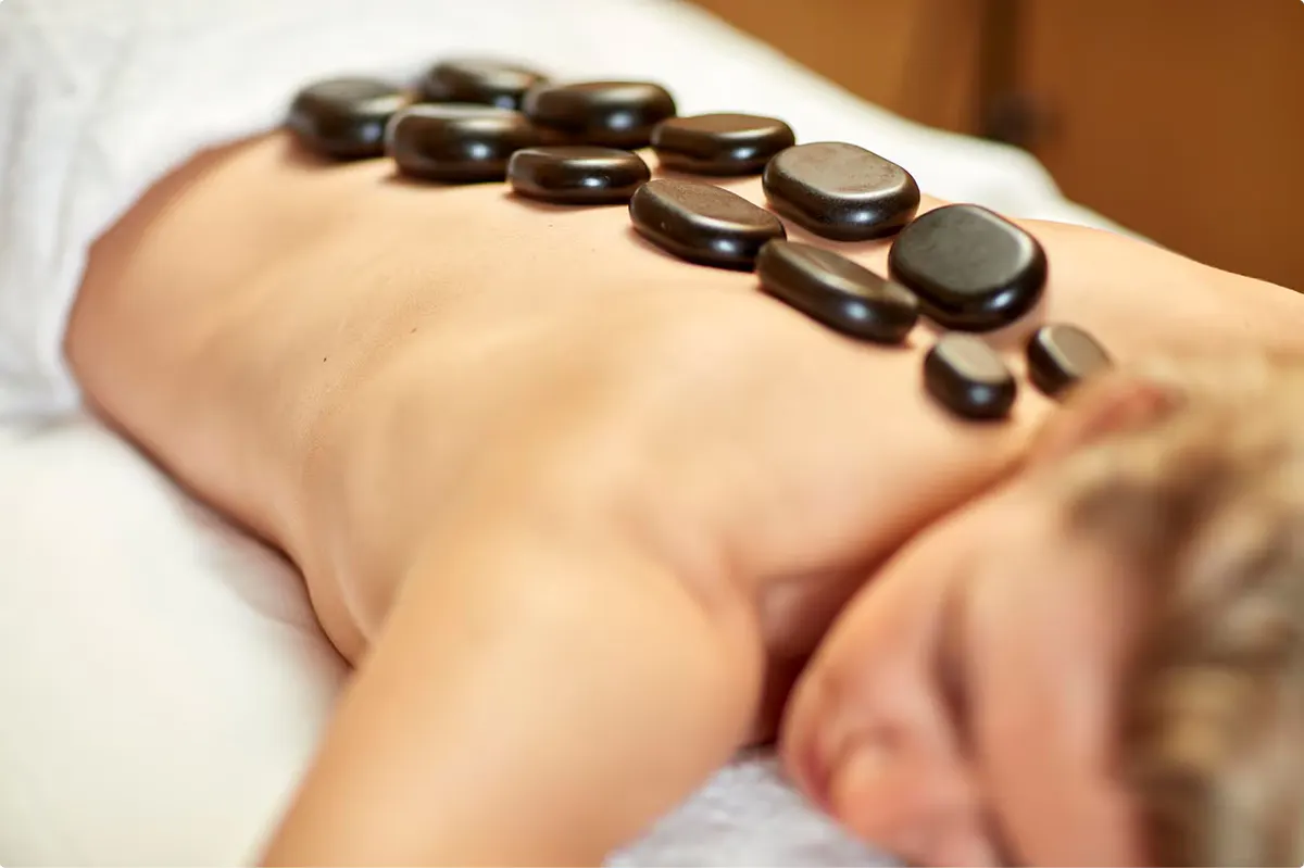 Hot stone therapy treatment being applied to client’s back with therapist’s hands