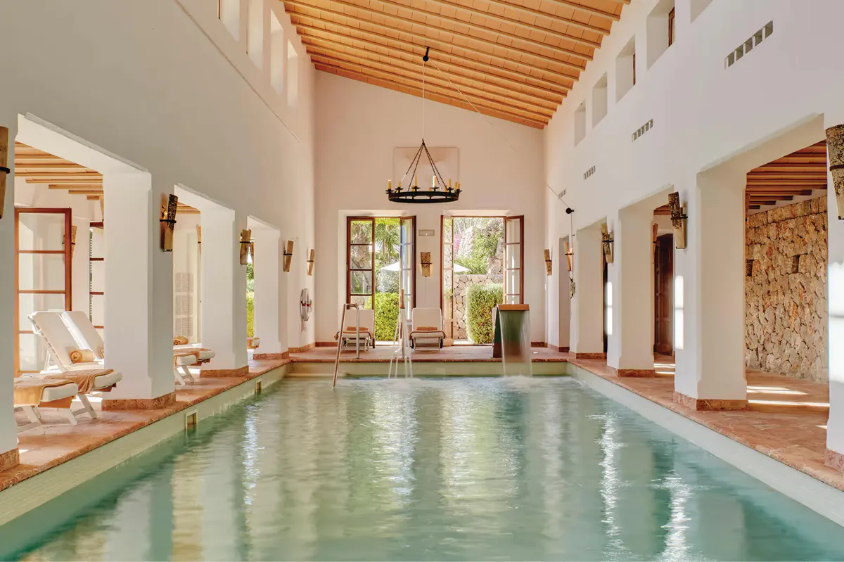 Indoor swimming pool with wooden ceiling, cream stone columns, and natural light
