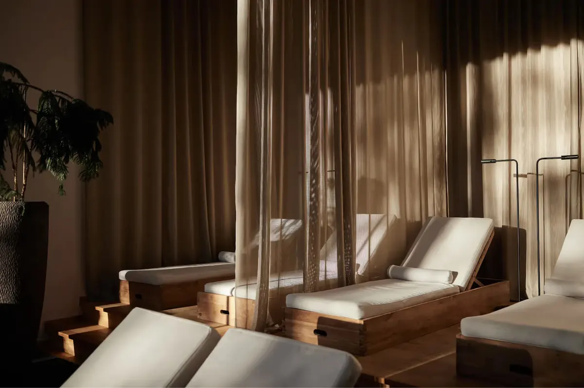 Spa lounge area with wooden sun beds and floor-to-ceiling windows casting dramatic light