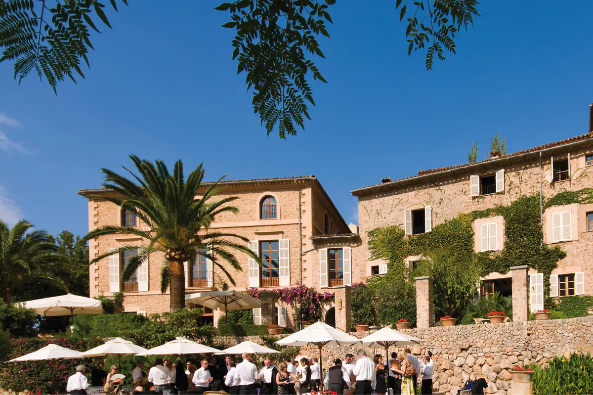Stone manor buildings with palm tree, outdoor seating area, and Mediterranean landscape