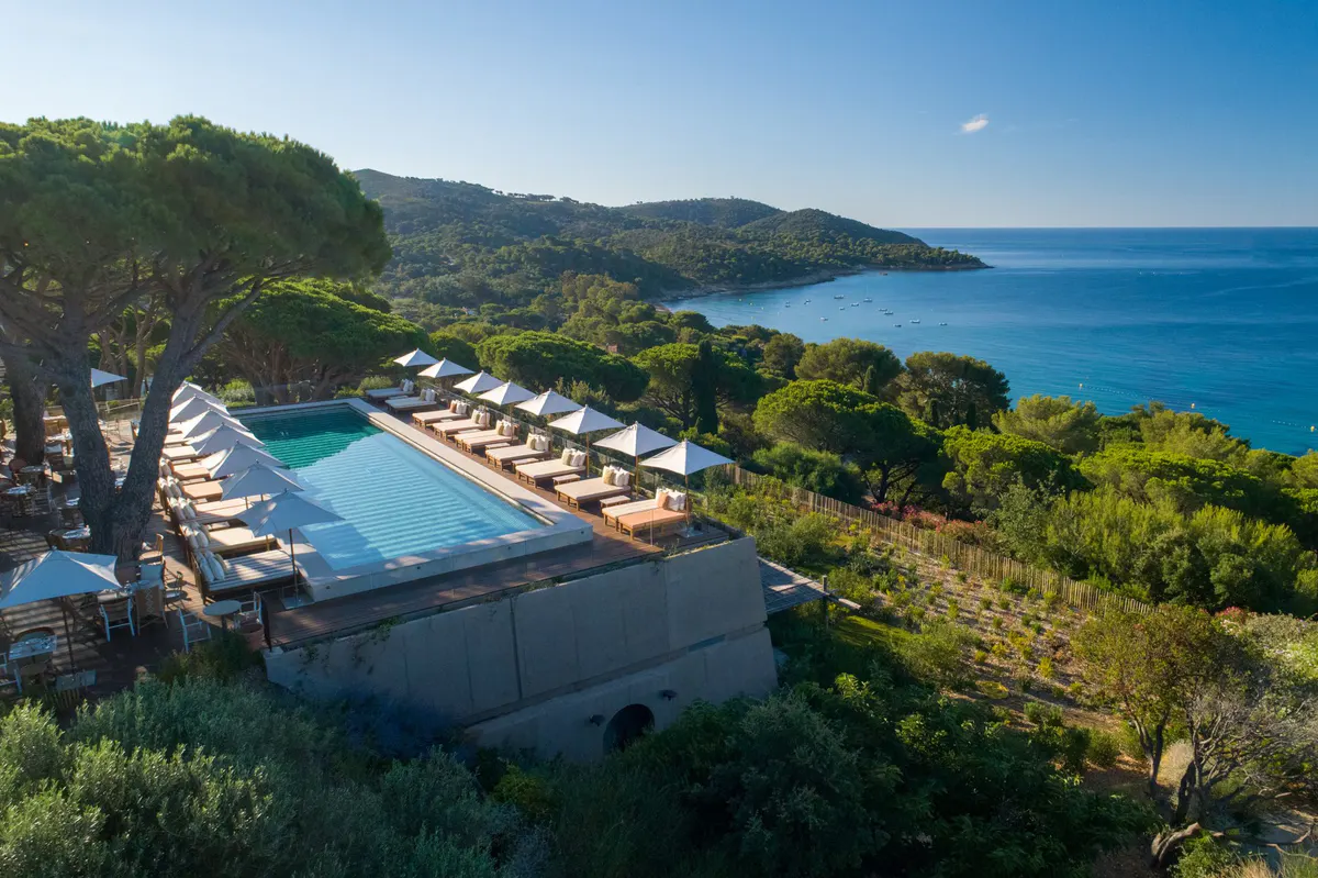 Pool with loungers and umbrellas on cliff overlooking blue Mediterranean
