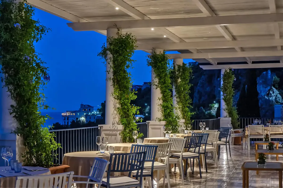 Contemporary covered dining area at night with ivy pillars and Mediterranean seascape
