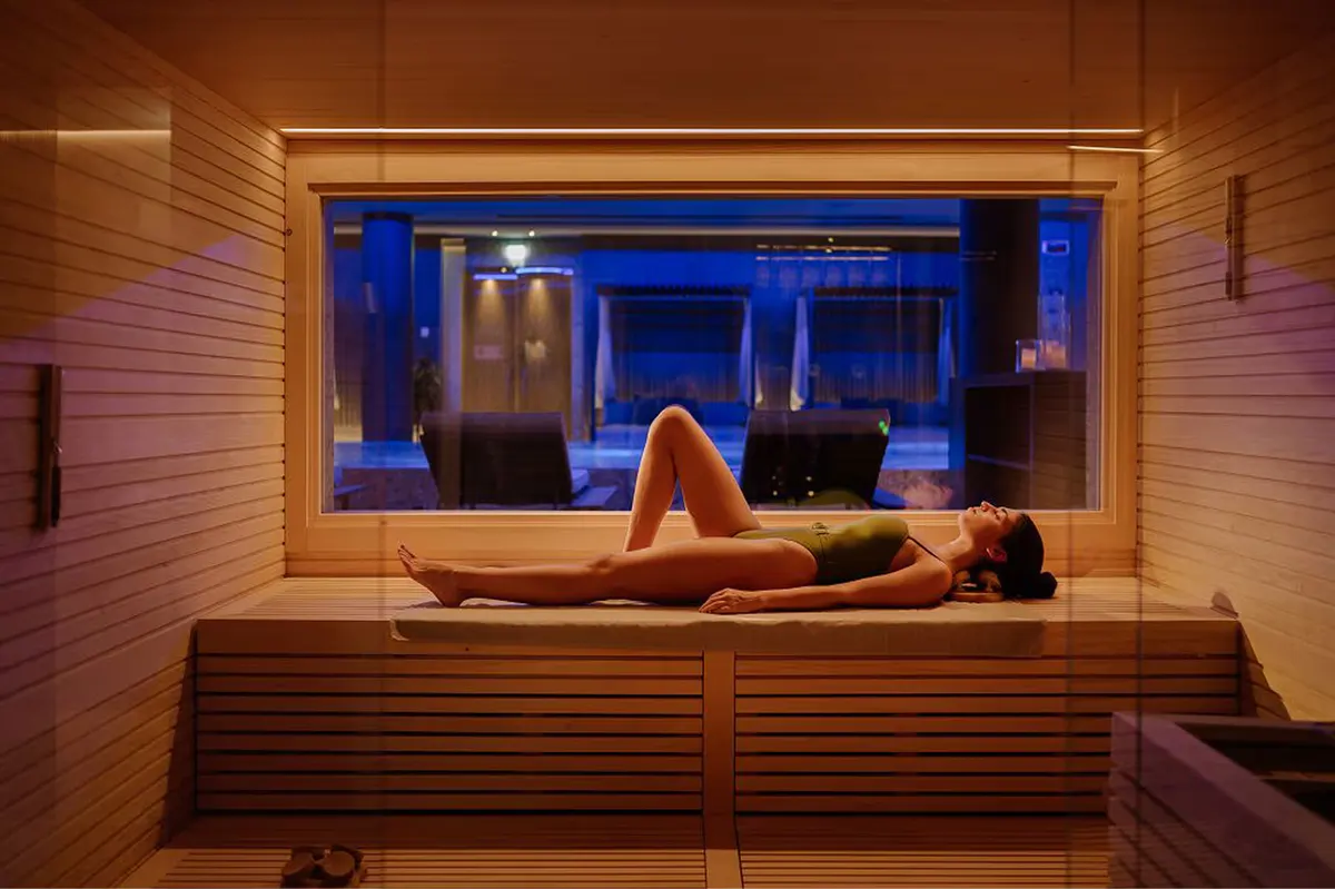 A spa room with a woman in a plunge pool surrounded by wood and blue light
