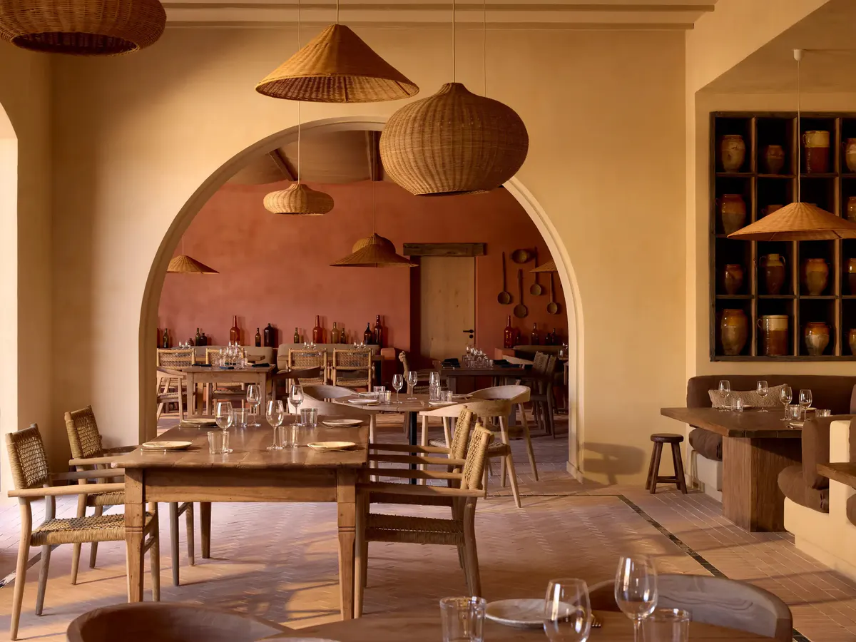 Woven rattan pendants hang over a rustic dining room with a terracotta arch and wine bottles