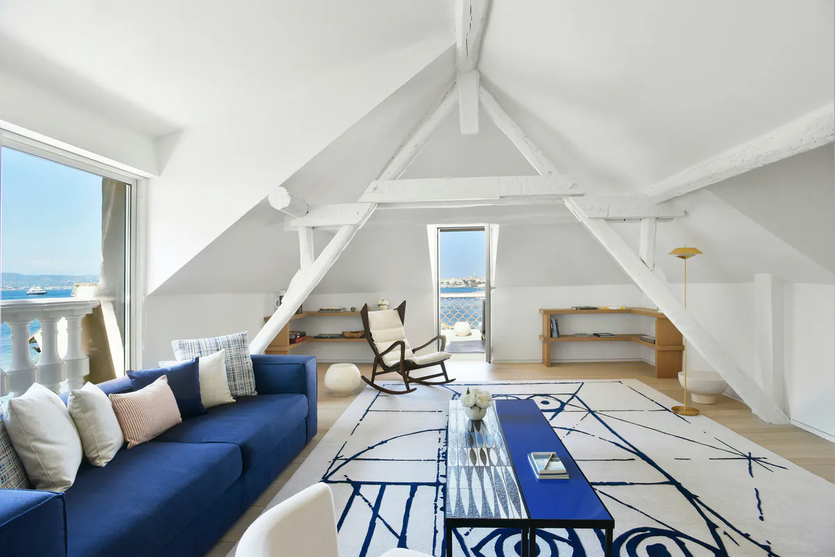 Vaulted white suite with blue sofa, patterned rug, and sea access