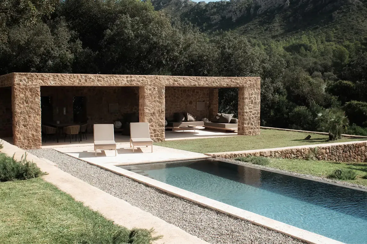 Stone pavilion structure with open walls framing a swimming pool in manicured estate garden